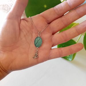 un collier à planter par modibulle, avec sa perle contenant des graines de tomates cerises et sa breloque en forme de paquerette. De couleur vert canard.